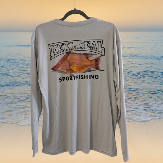 Long-sleeve shirt with fish graphic and 'Reel Deal Sportfishing' text on a beach background