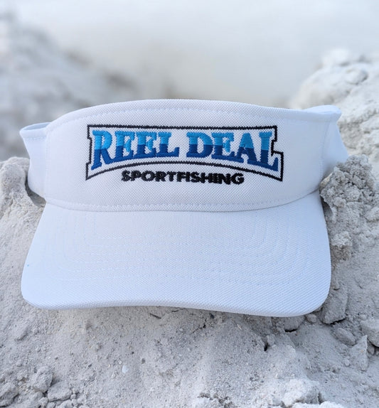 White visor with 'Reel Deal Sportfishing' logo on sandy background